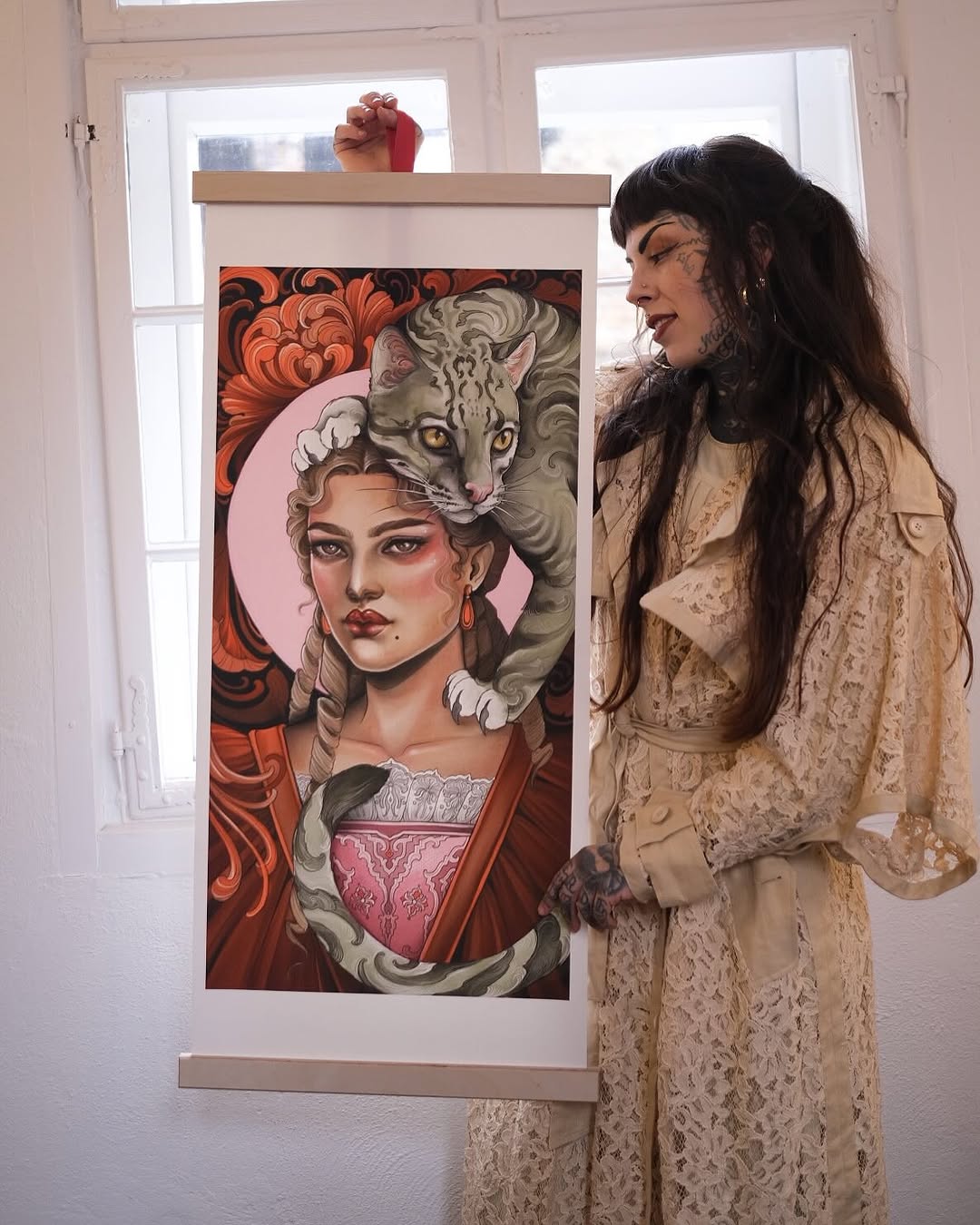 Framed artwork depicting a woman with braided hair and a cat draped across her shoulders, rendered in orange, pink, and grey tones.