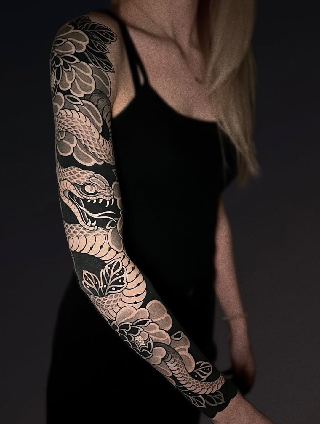 Full-sleeve arm tattoo featuring an ornate dragon with scaled body, floral patterns, and a demon mask in grayscale and tan tones.