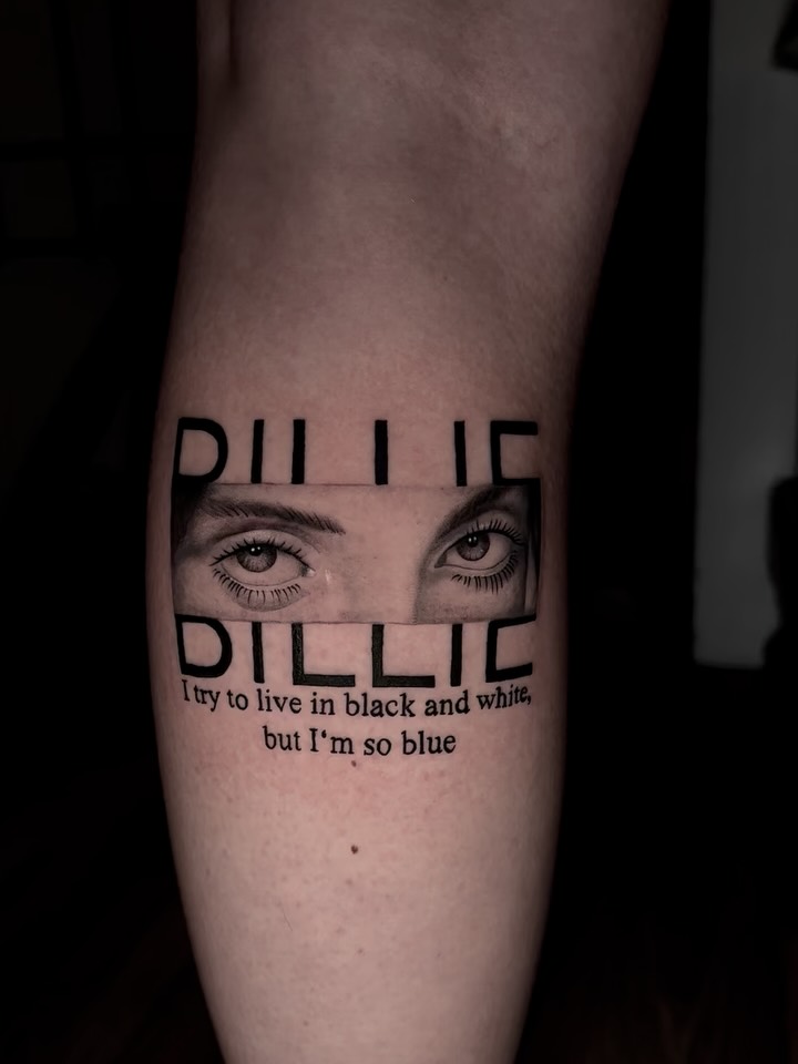 Billie Eilish tribute tattoo on forearm featuring her eyes and text "I try to live in black and white but I'm so blue" in black ink.