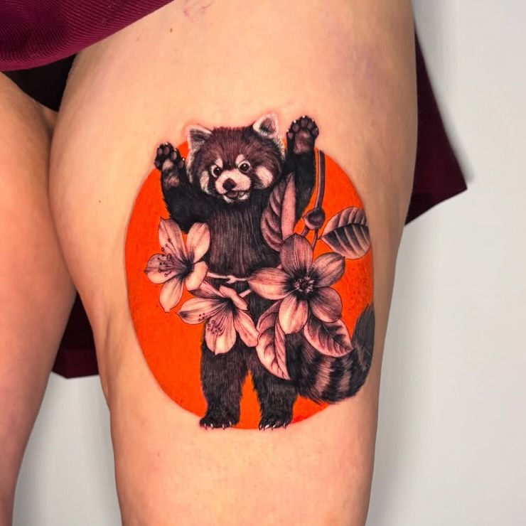 Red panda with raised paws holding pink flowers against a bright orange circular background, tattooed on the thigh.