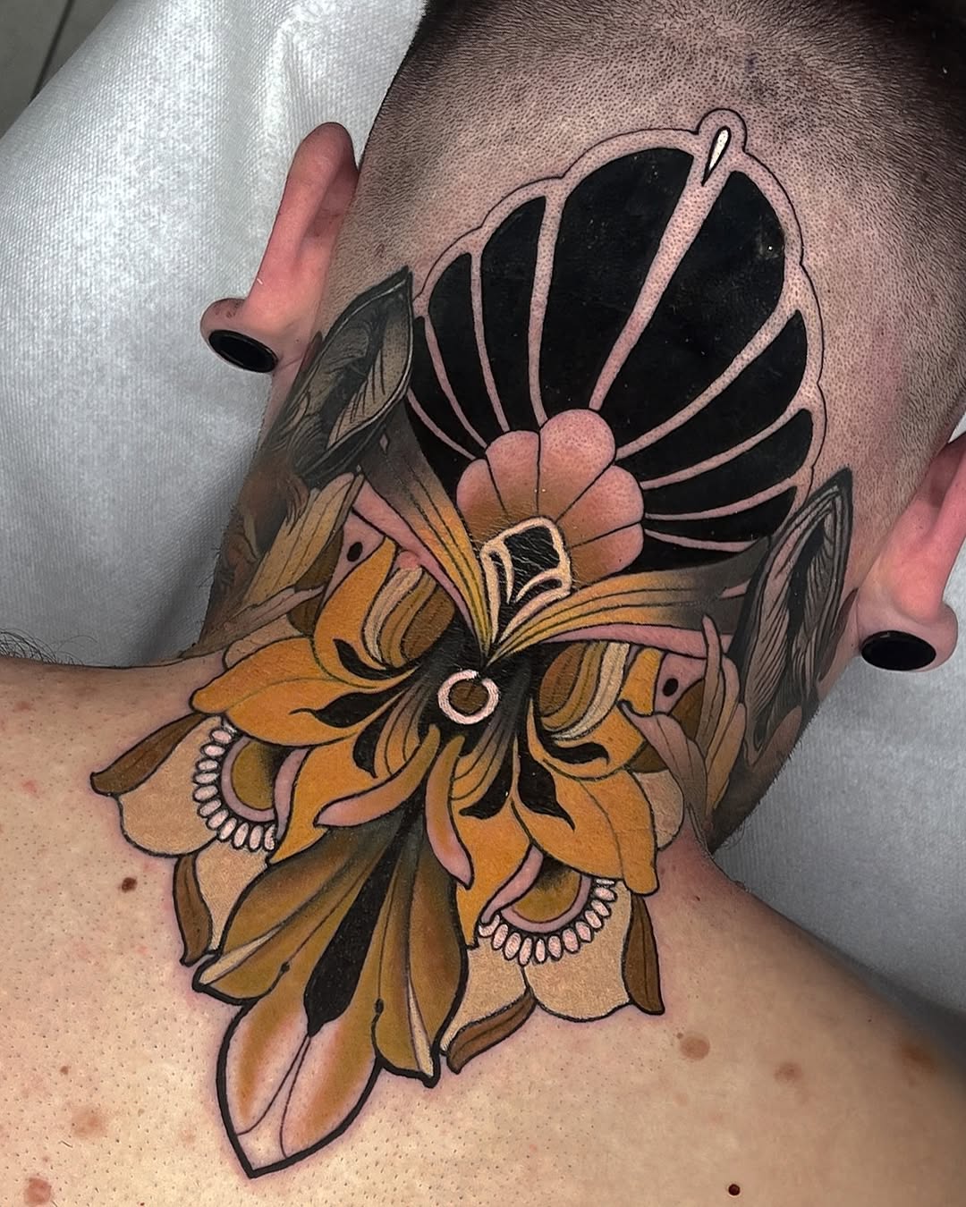 Colorful floral tattoo on forearm featuring layered petals in gold, orange, and black with decorative circular elements and fine line details.