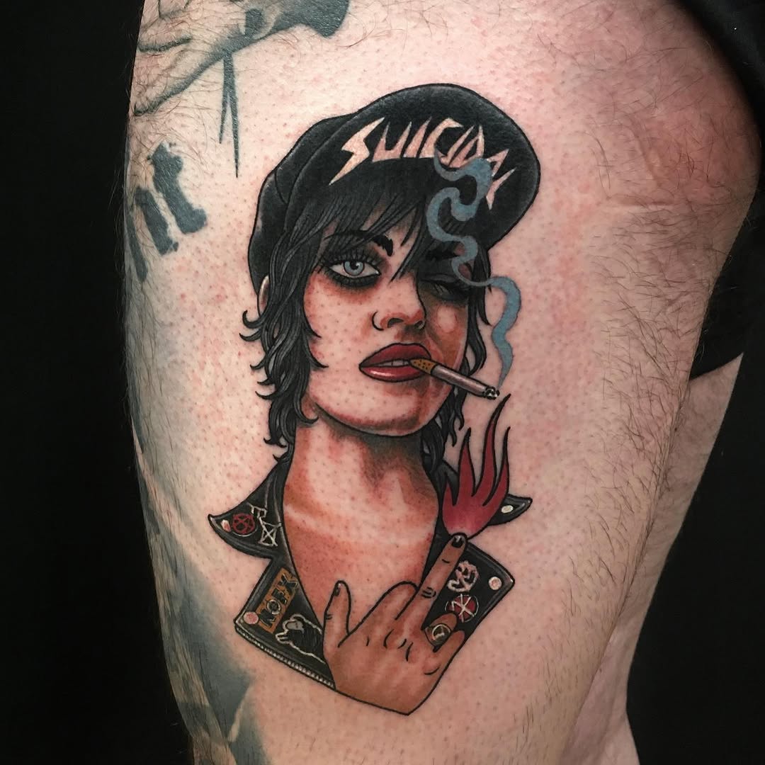 Colored shoulder tattoo depicting a person with black hair and hat, smoking a cigarette, wearing studded jacket with red and flesh tones.