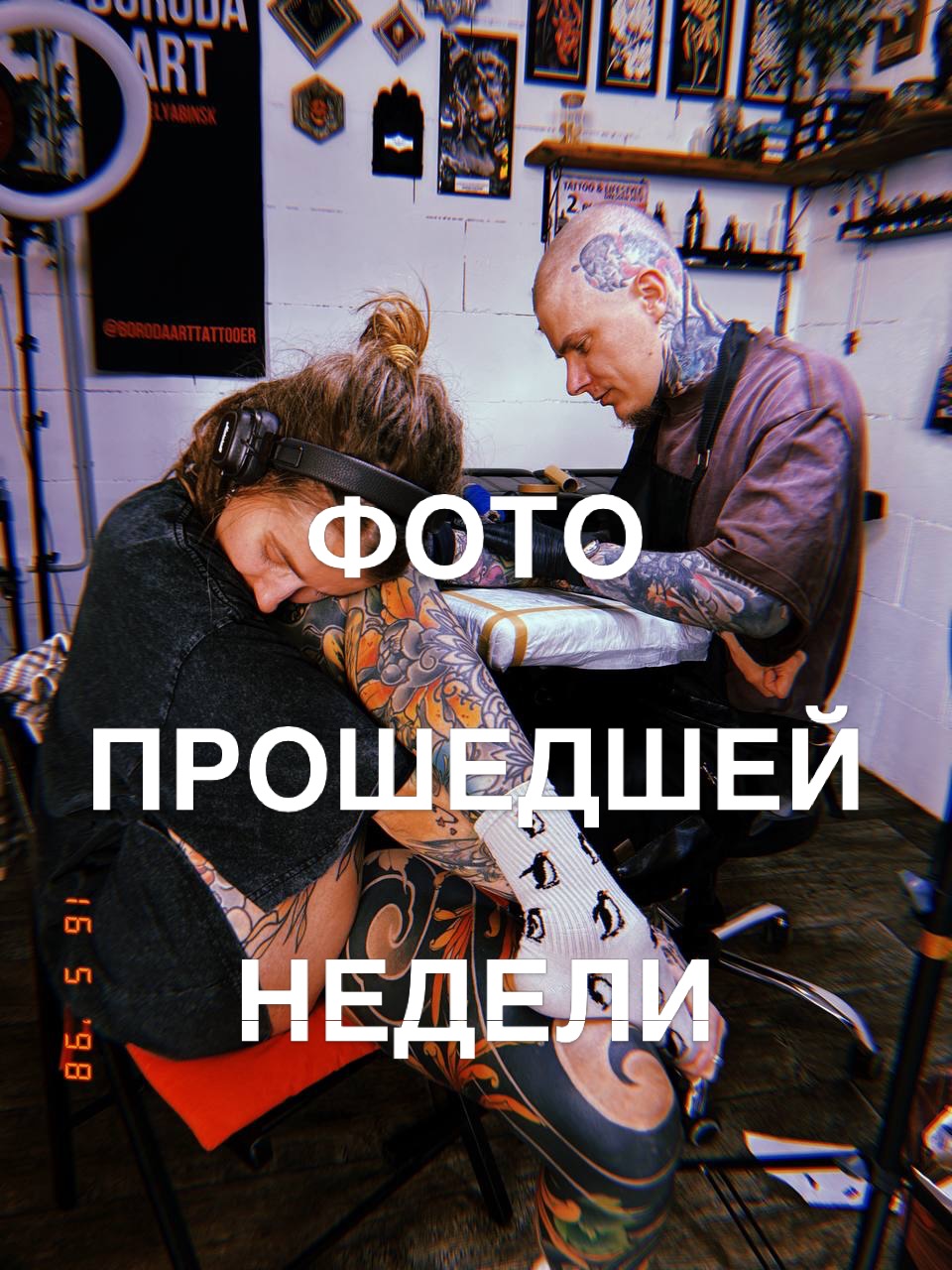 Tattoo artist applies orange and black designs to client's arm and leg in studio setting with artwork displayed on walls.