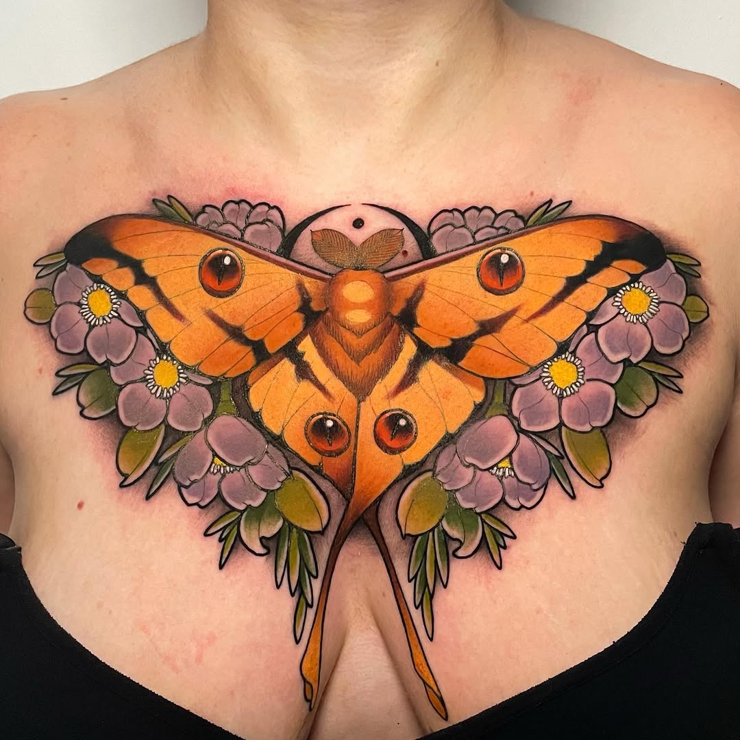 Symmetrical orange moth with eye markings and long tail feathers, surrounded by purple flowers with yellow centers, tattooed on chest.