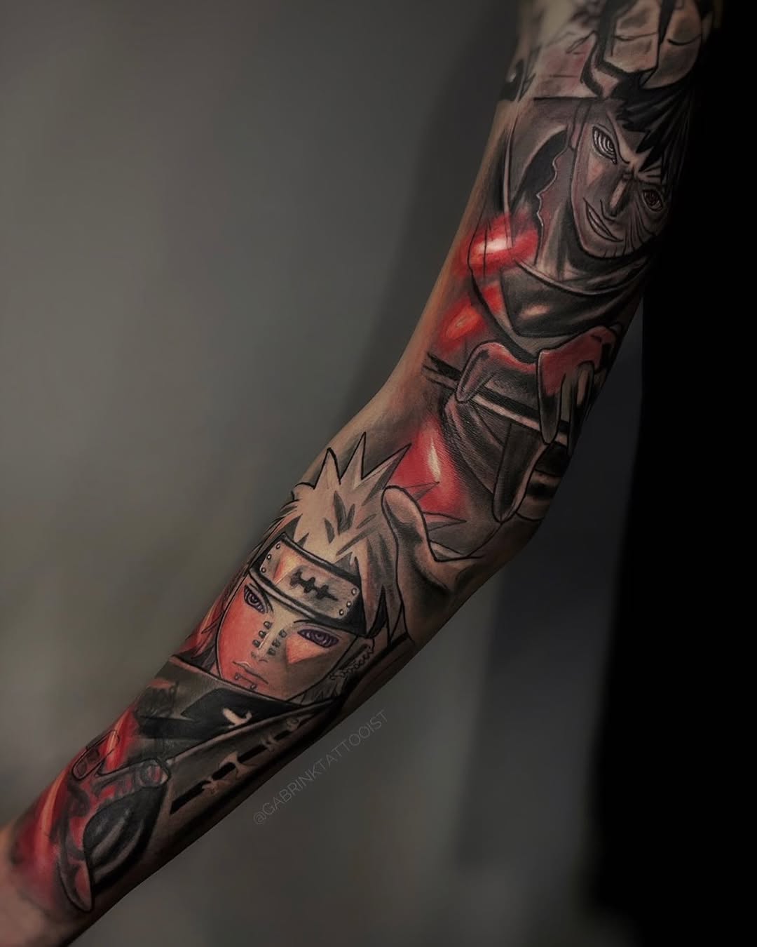 Full-sleeve arm tattoo featuring red and black ink with character portraits, spiky-haired figures, and geometric designs running from shoulder to wrist.