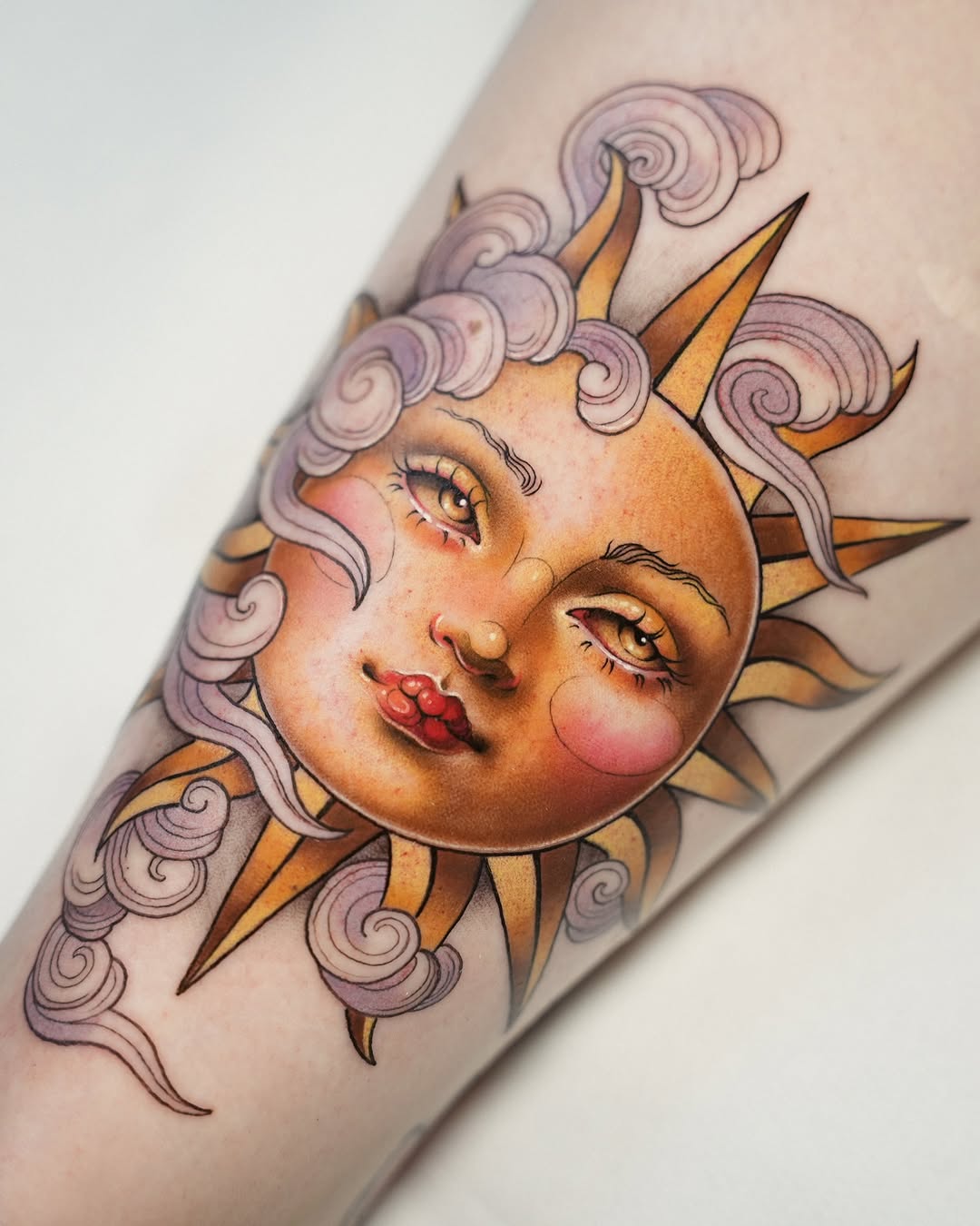Colorful tattoo on forearm featuring a smiling celestial face with purple curled hair, golden sun rays, closed eyes, and rosy cheeks.
