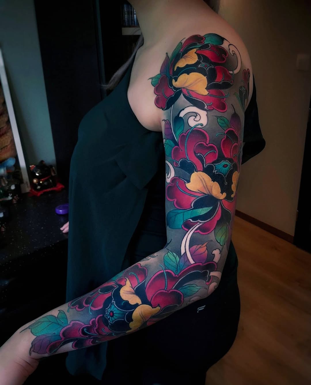 Full-sleeve floral tattoo featuring red, yellow, teal, and purple flowers with ornamental scrollwork on a person's arm.
