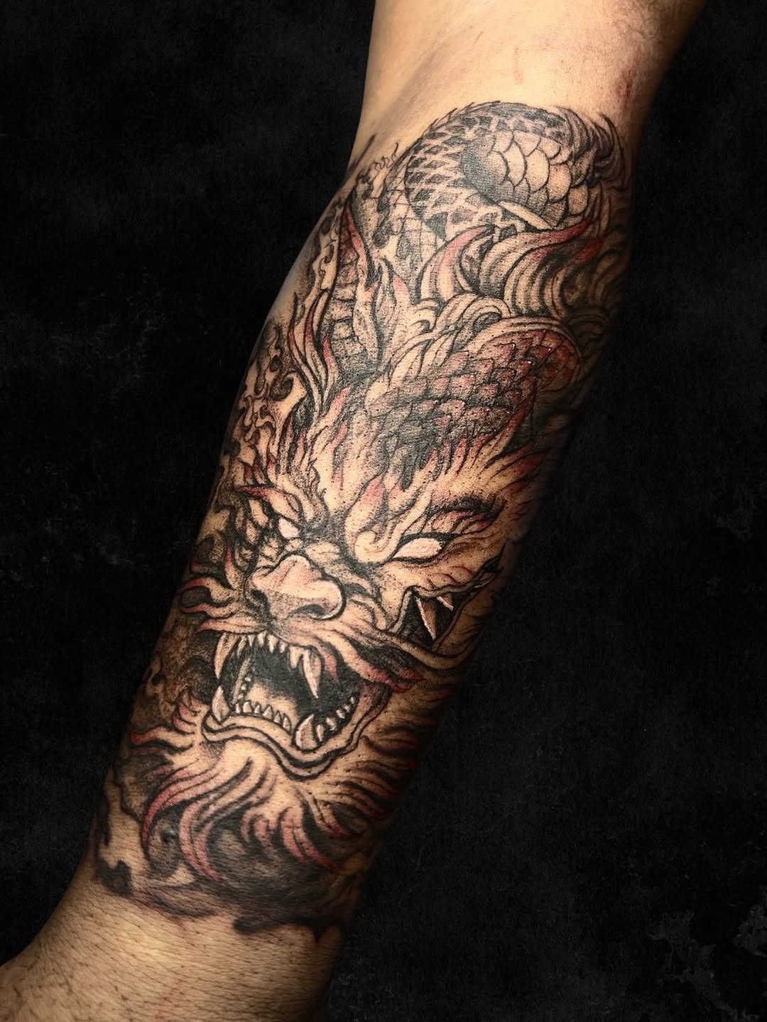 Dragon and skull tattoo wrapped around the forearm in black ink with red and grey shading detail.