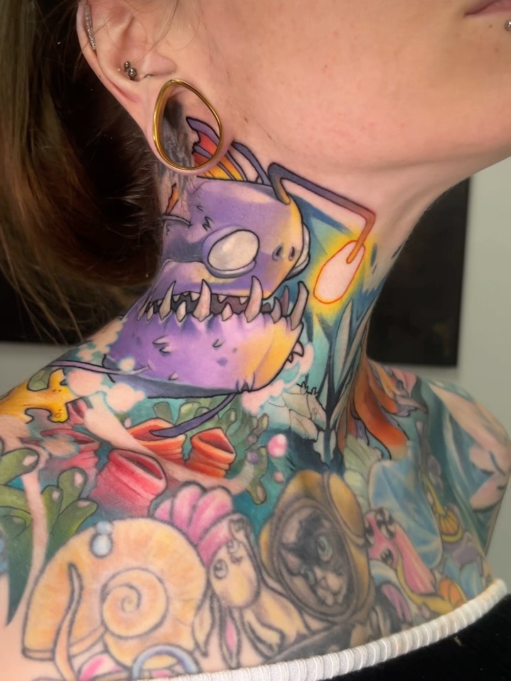 Colorful neck and chest tattoo featuring a purple monster with large eyes, surrounded by vibrant flowers and abstract designs in yellow, pink, green, and blue.