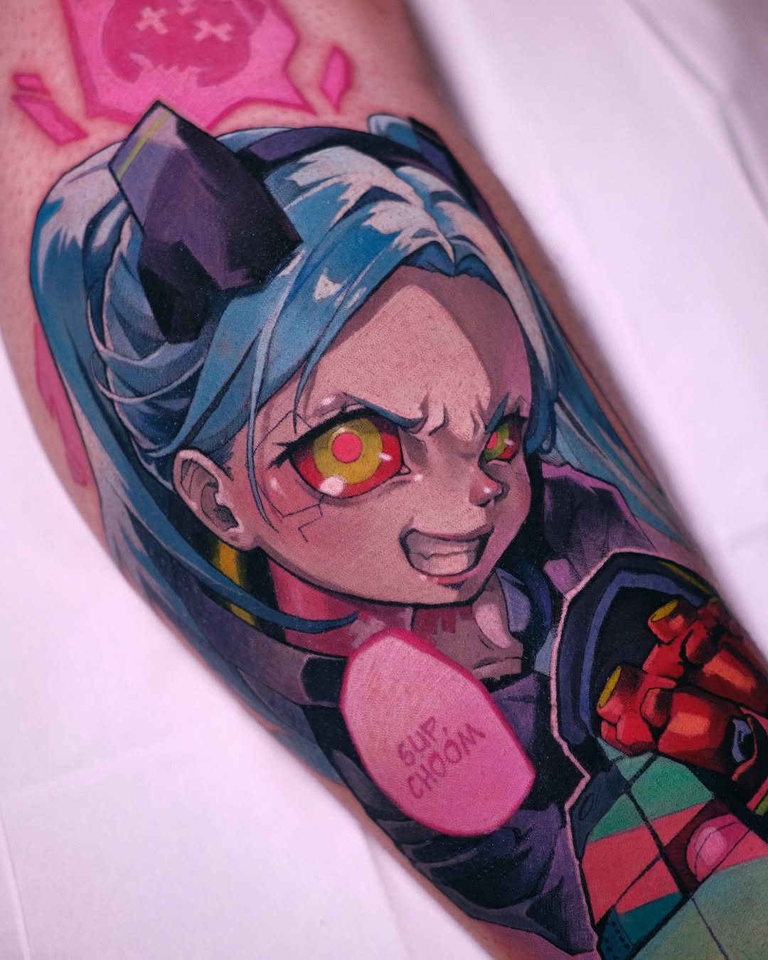 Colorful portrait tattoo of a character with blue hair, red and gold eyes, and dark clothing on an upper arm.