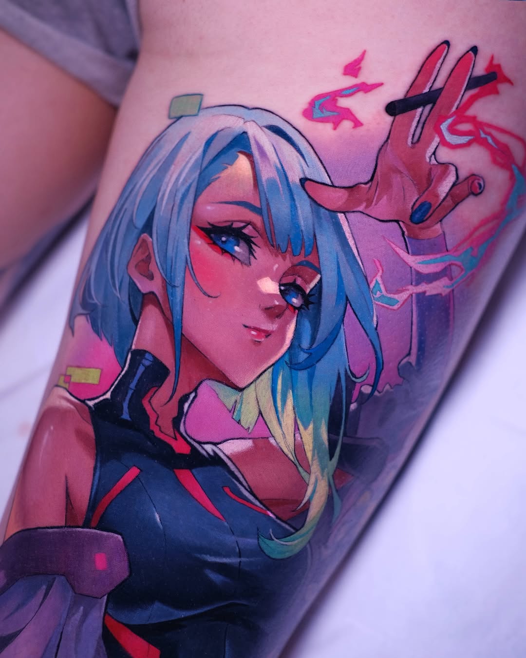 Colorful shoulder tattoo featuring a blue-haired character with pink and red skin tones, geometric elements, and glowing eye details in vibrant magenta, blue, and black.