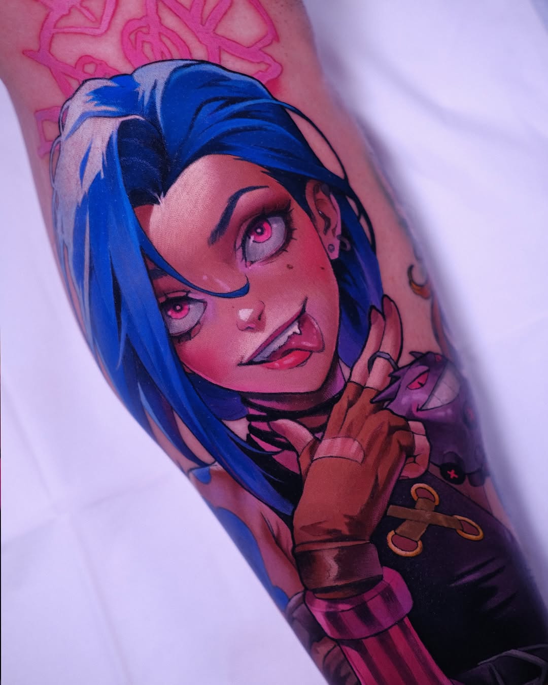 Colorful tattoo on an arm featuring a female character with blue hair, pink skin, and expressive eyes wearing dark clothing with gold accents.