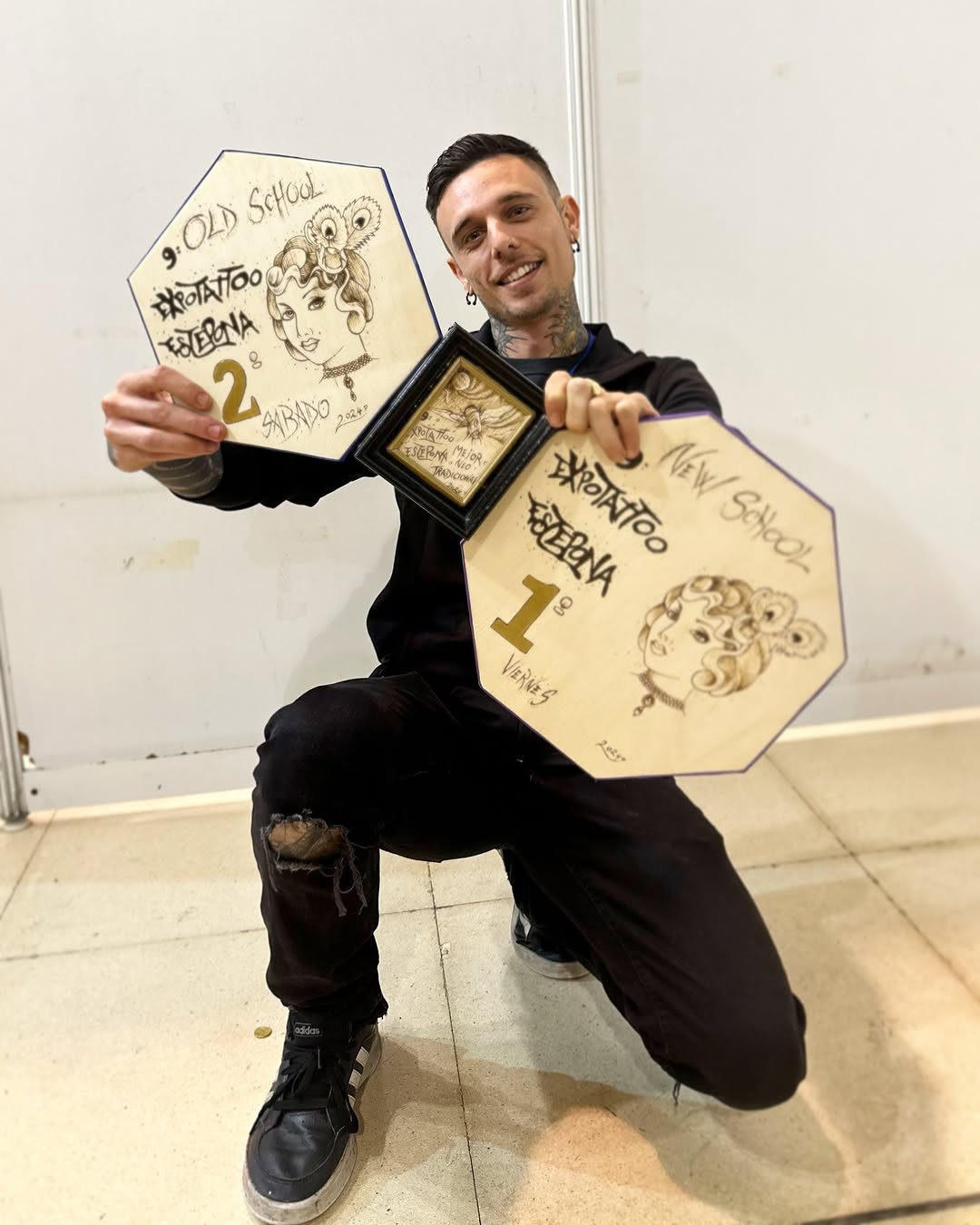 Tattooed man holding framed hexagonal sketches featuring portrait illustrations and decorative elements in black ink on cream-colored paper.