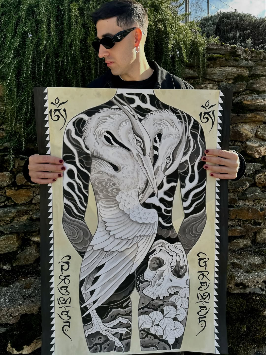 Detailed elephant head and skull tattoo design with ornamental patterns and Sanskrit text on cream paper, held by artist outdoors.