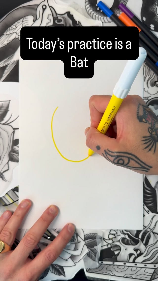 Tattoo artist demonstrates bat drawing technique using yellow marker on white paper during a practice session.