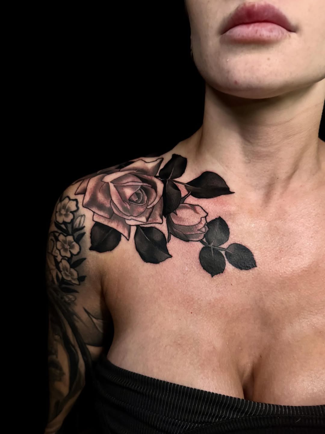 Rose and leaf tattoo on the shoulder and chest of a shirtless person, featuring pink and black ink with detailed shading.