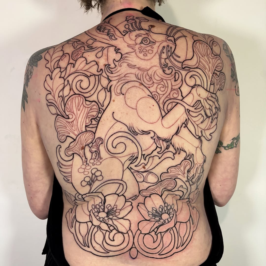 Back tattoo featuring ornate scrollwork, floral motifs, and a lion figure with decorative elements in black and red ink.