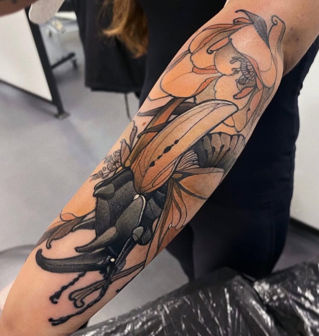 Colorful insect and flower tattoo sleeve on an arm featuring orange, black, and tan shading with detailed botanical elements.