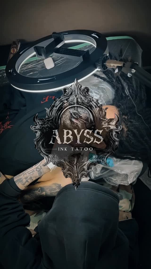 Ornate decorative frame with "ABYSS INK TATOO" text and skull imagery tattooed on upper arm in black and grey ink.