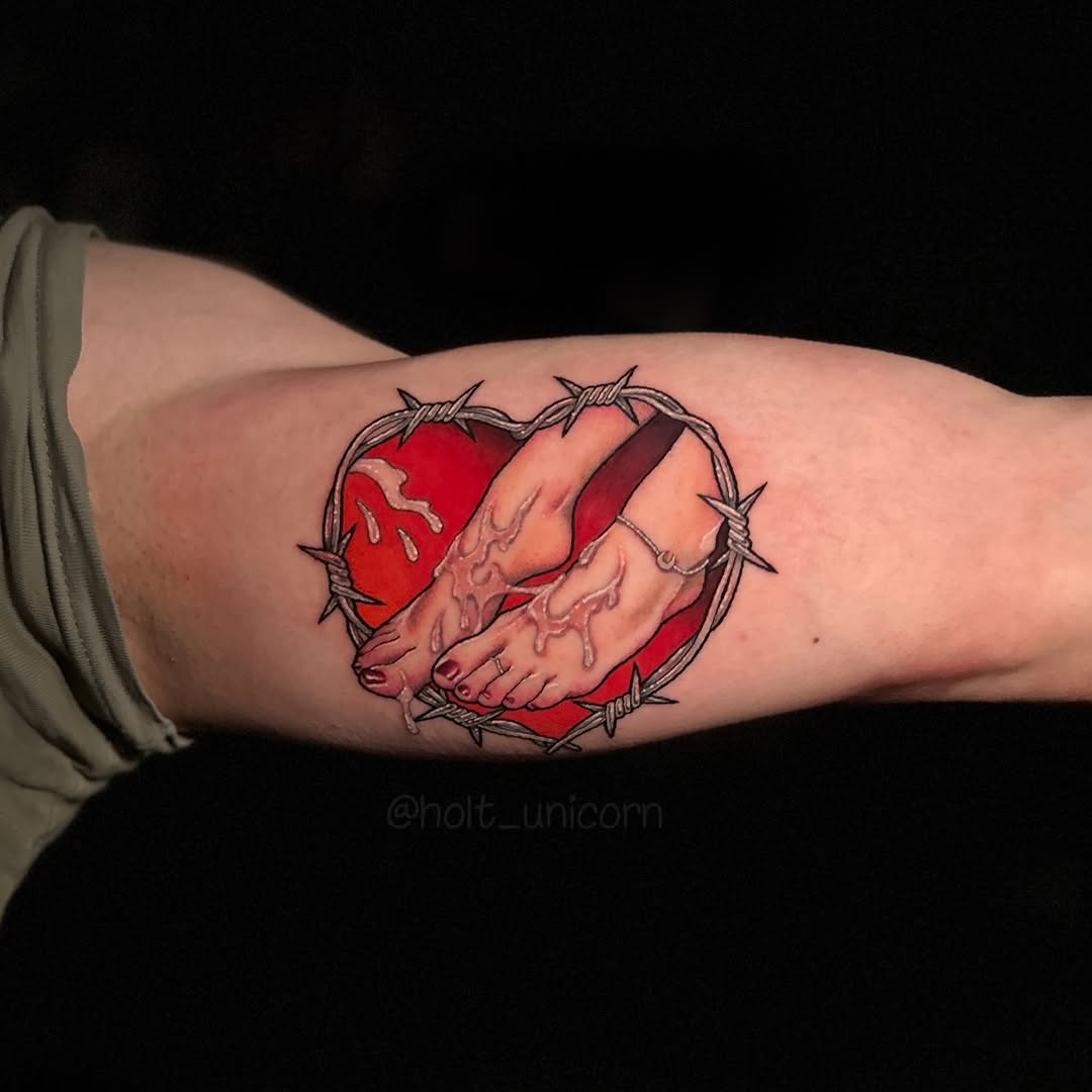Anatomical hands clasped together in red and flesh tones, surrounded by a thorned circular wreath, tattooed on the upper arm.
