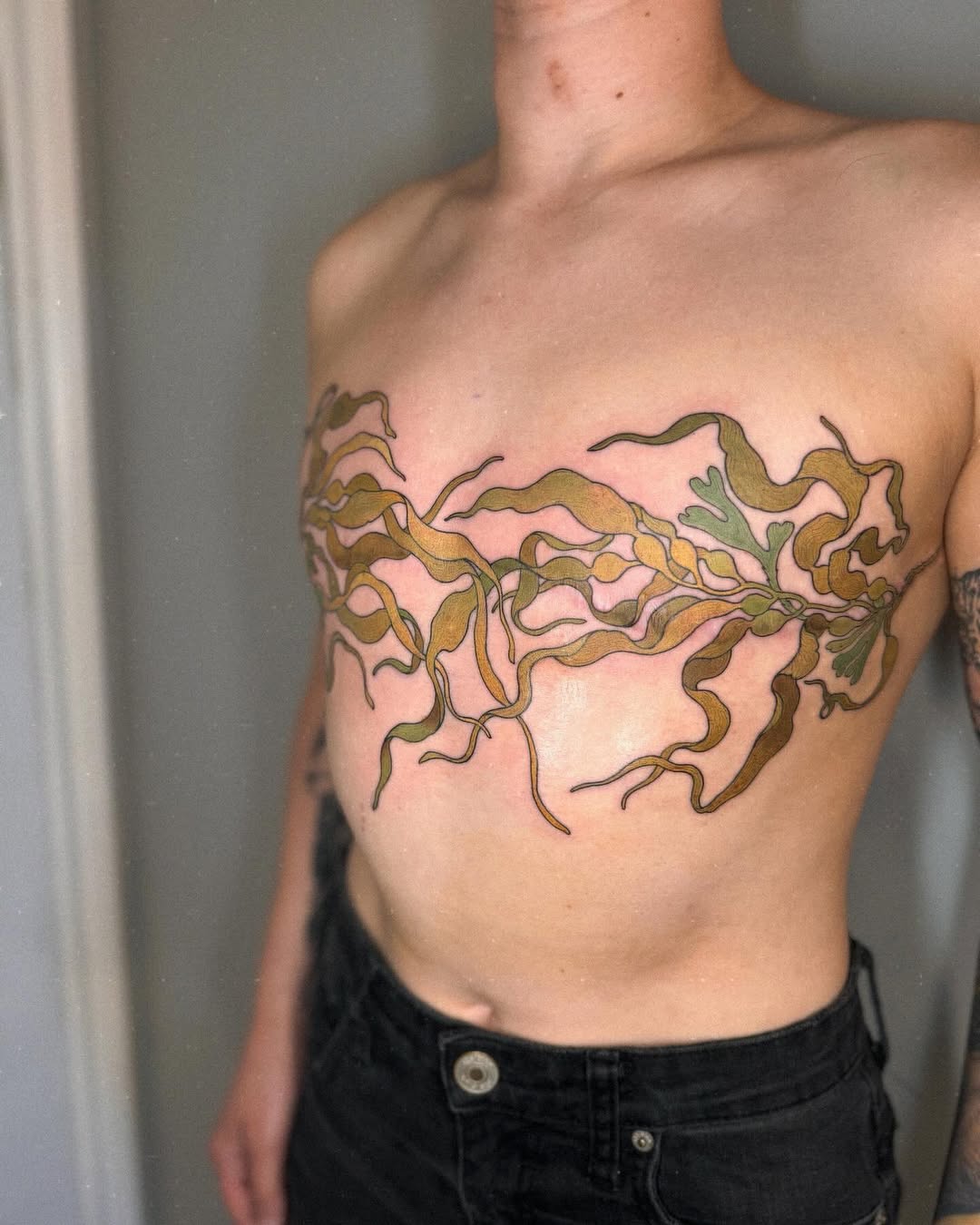 Colorful organic tentacle or seaweed design in brown, green, and tan wrapping across the chest in a horizontal band.