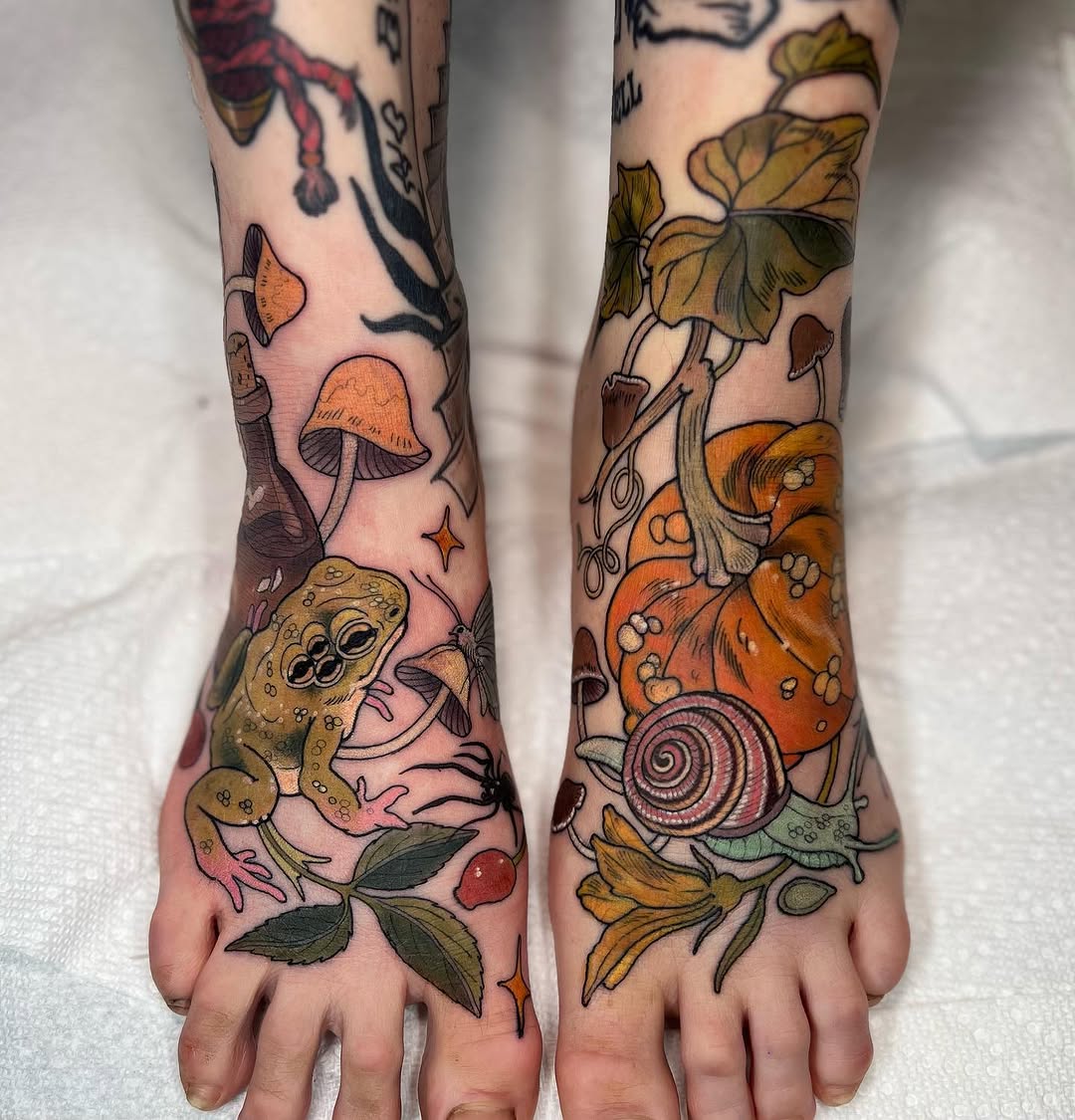 Two feet displaying colorful tattoos of mushrooms, toads, snails, flowers, leaves, and botanical elements in orange, green, brown, and purple hues.