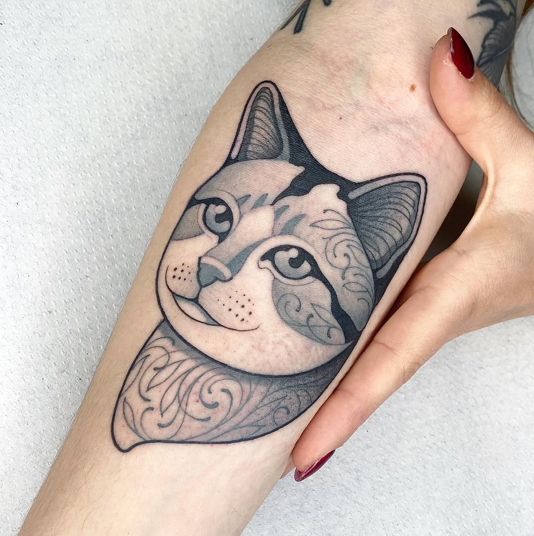 Cat head tattoo on forearm with decorative swirl patterns, black ink with shading, displayed on pale skin with red nail polish visible.