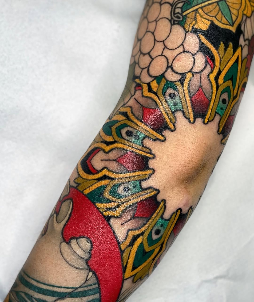 Colorful tattoo on an arm featuring stacked dragon heads with red scales, yellow ornamental details, and green accents against skin-tone backgrounds.