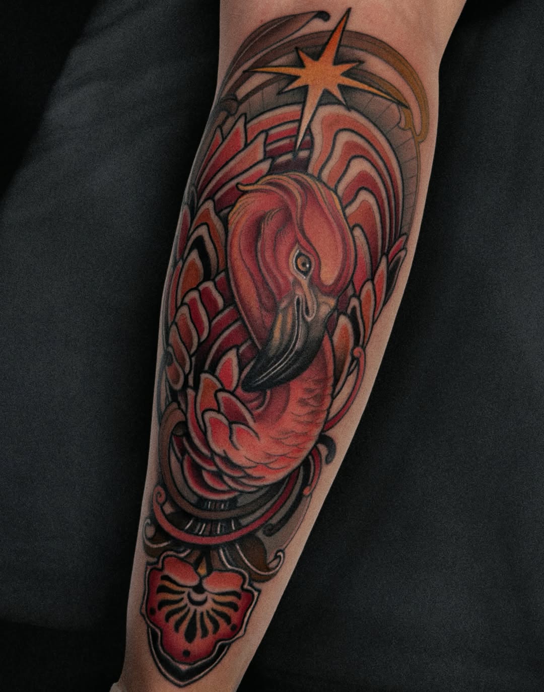 Colorful leg tattoo featuring a sacred heart with radiating rays, ornamental shell motif below, and star symbol at top in red, orange, and brown tones.
