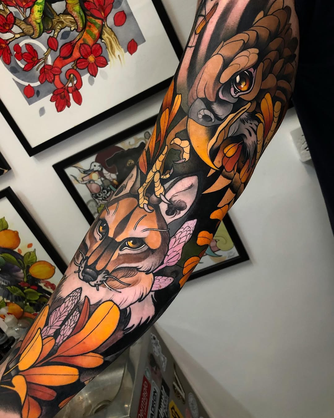Colorful arm sleeve tattoo featuring a deer's head and owl surrounded by orange flowers and pink petals on dark background.