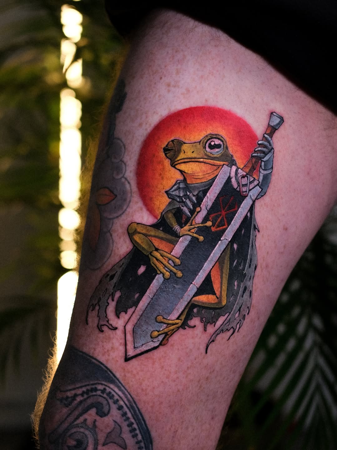 Anthropomorphic frog wearing black outfit and holding a sword, positioned on upper thigh with red and orange circular background.