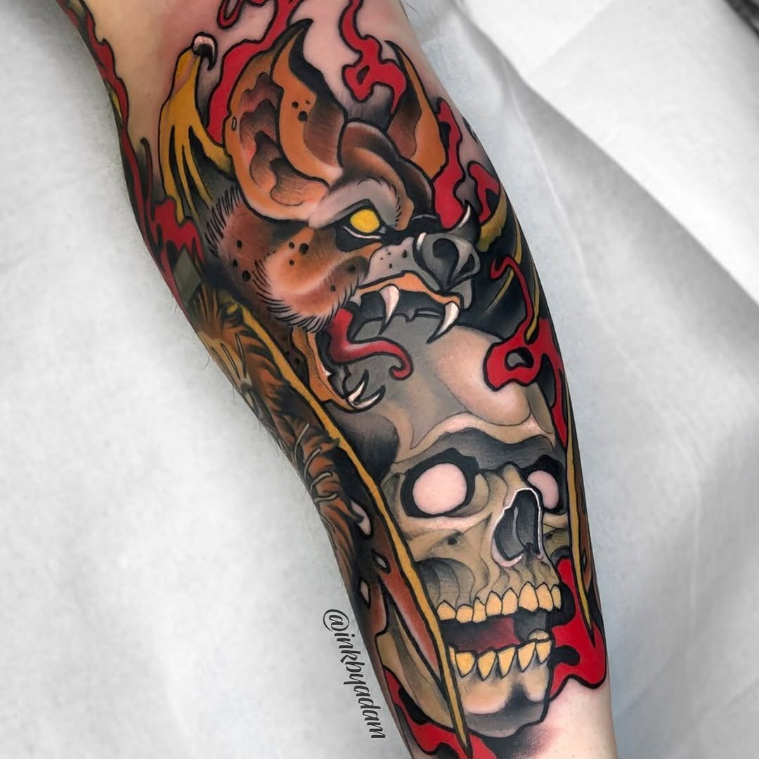 Colorful arm tattoo featuring a demon face above a skull with flames, rendered in red, orange, yellow, and black.