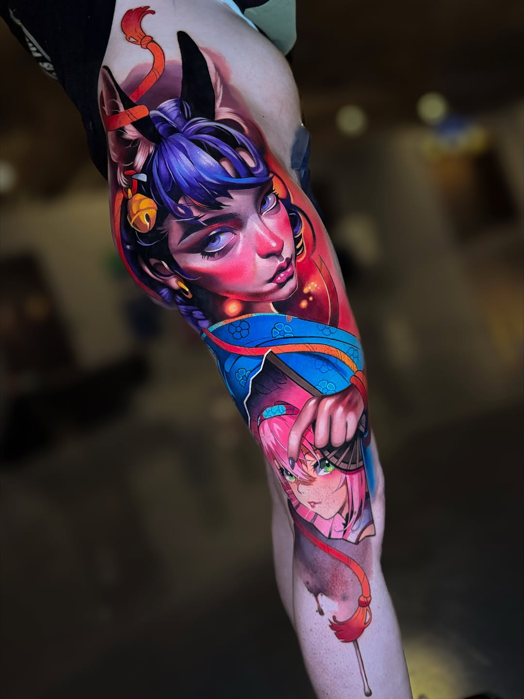 Colorful leg sleeve tattoo featuring two stylized female faces with purple hair, horns, and demonic features, surrounded by red serpents and blue ornamental bands.