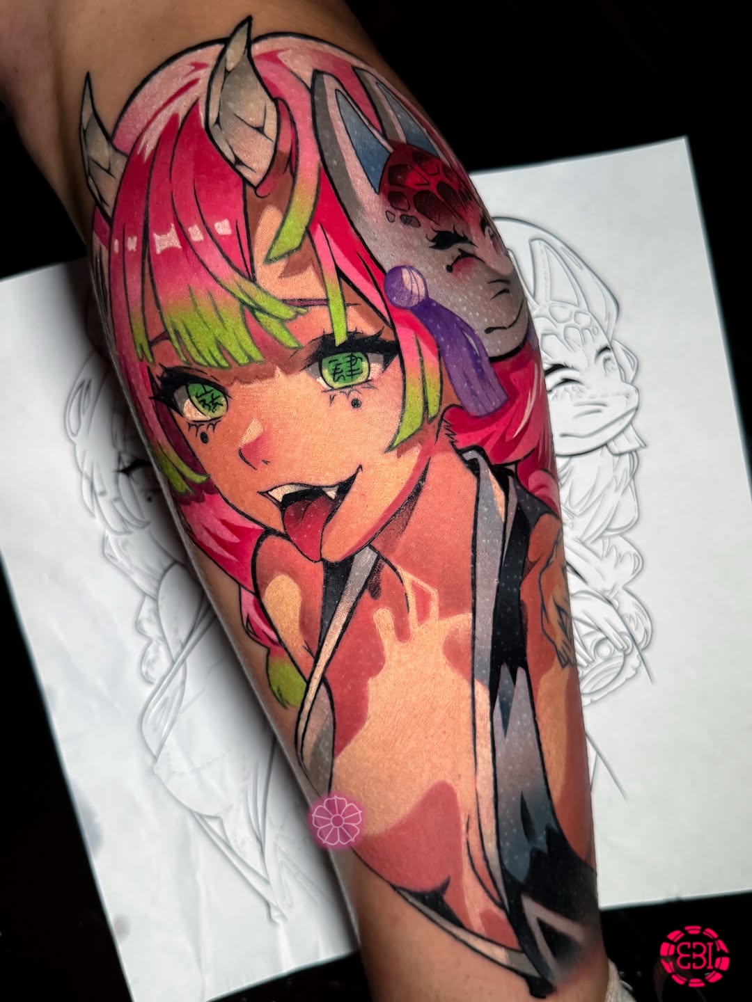 Colorful portrait tattoo on upper arm featuring a character with red and lime green hair, green eyes, horns, and wearing dark clothing against a white reference sheet background.
