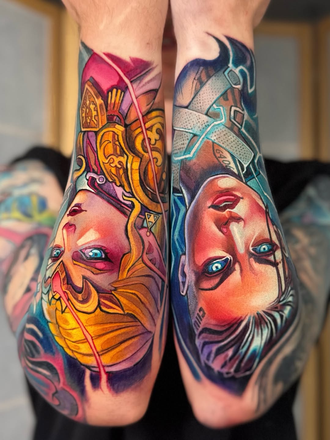 Two colorful mask faces with elaborate headdresses on both calves feature vibrant reds, golds, blues, and purples with striking eyes and ornamental details.