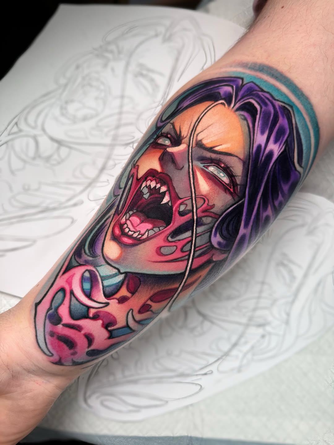 Colorful portrait tattoo on forearm featuring a person with purple hair, open mouth, and pink, orange, and teal tones with decorative swirling elements.