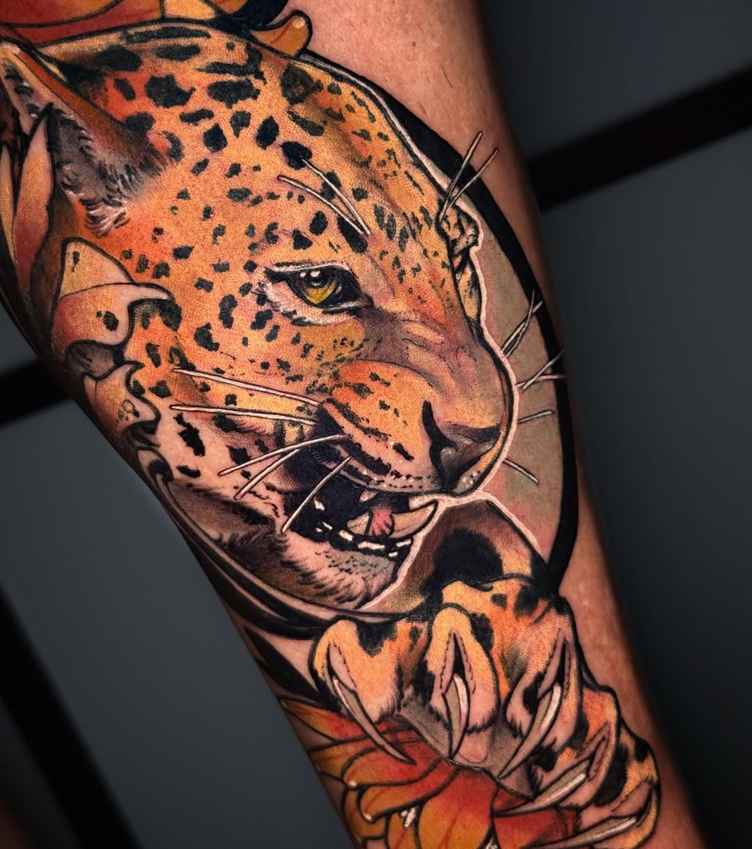 Spotted leopard head with yellow eyes and whiskers on upper arm, surrounded by orange and red flowers at the base.