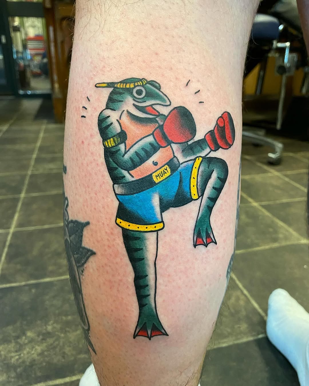 Colorful boxing kangaroo tattoo on calf with green skin, red boxing gloves, blue shorts, yellow accents, and red feet.