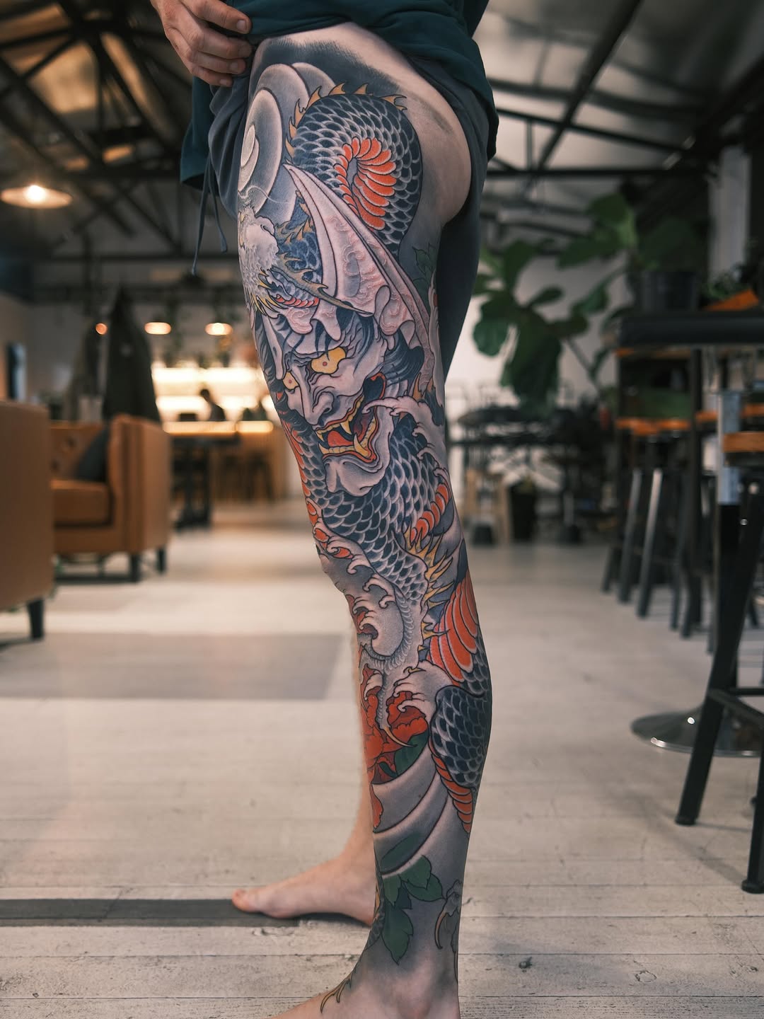 Full-leg tattoo sleeve featuring a large koi fish with red and orange fins, demon mask, and ornamental waves in gray, black, and red tones.
