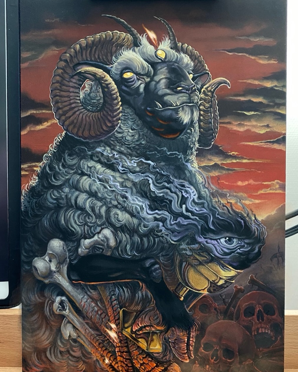 Detailed demon head tattoo design featuring multiple faces with curved horns, glowing eyes, ornate armor, and skulls against a dramatic sunset sky backdrop.