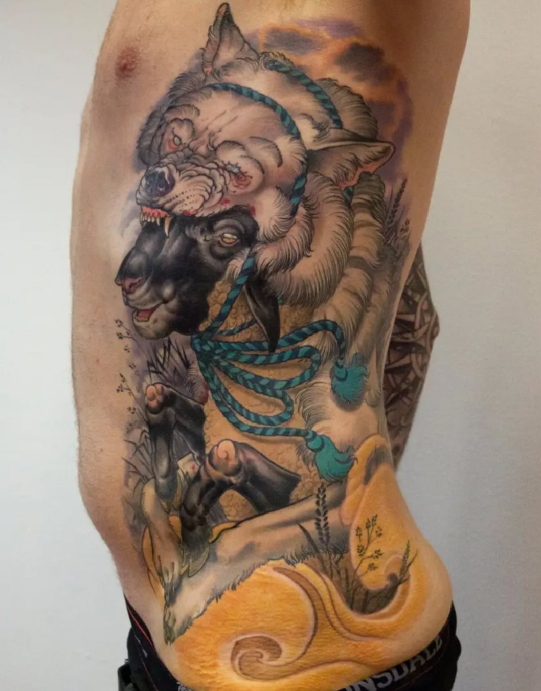 Colorful tattoo on the torso featuring mythical creatures with serpents, displaying teal, gold, and earth tones across the ribs and side.