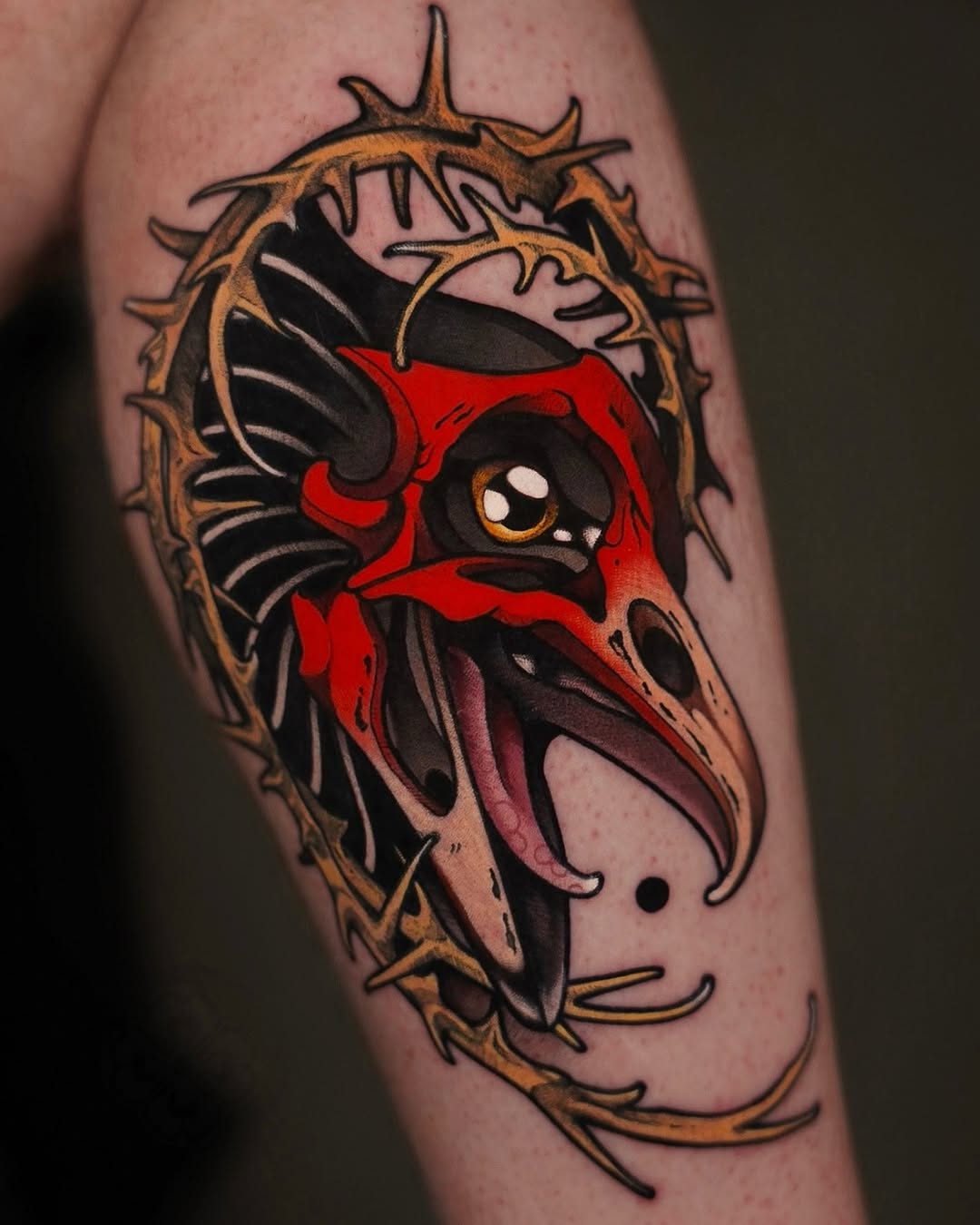 Colorful demon or oni mask face tattoo with red markings, golden horns, and black wing details on upper arm.
