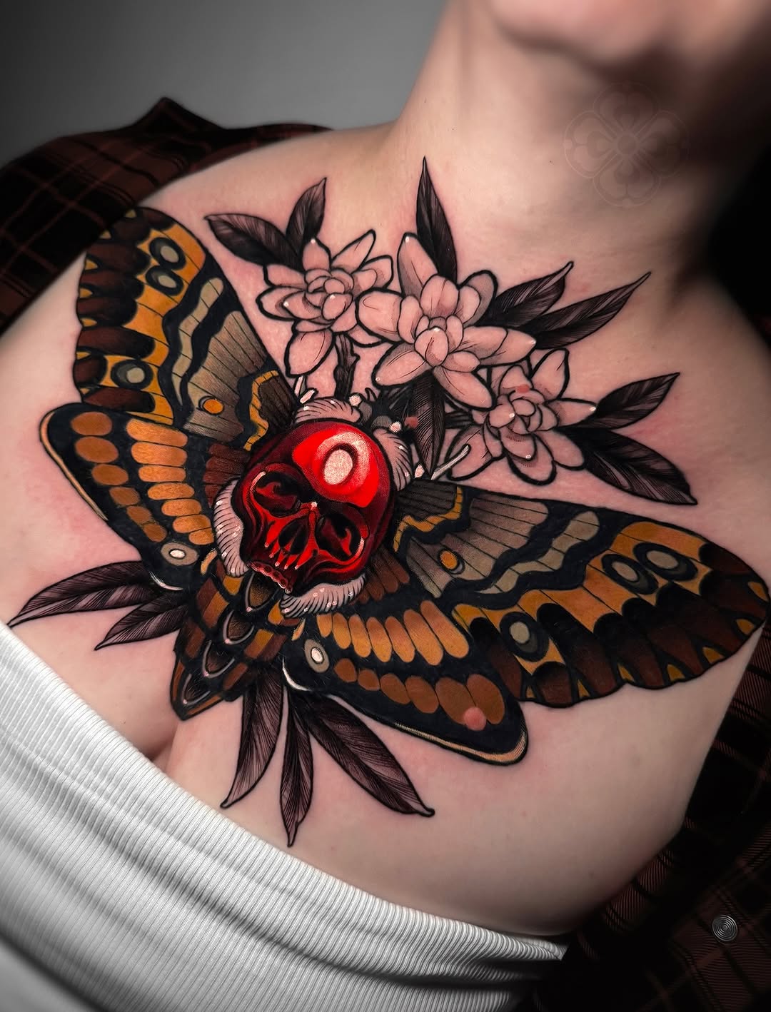 Colorful shoulder tattoo featuring a large butterfly with orange and black patterned wings, a red skull centerpiece, and pink flowers with dark leaves.