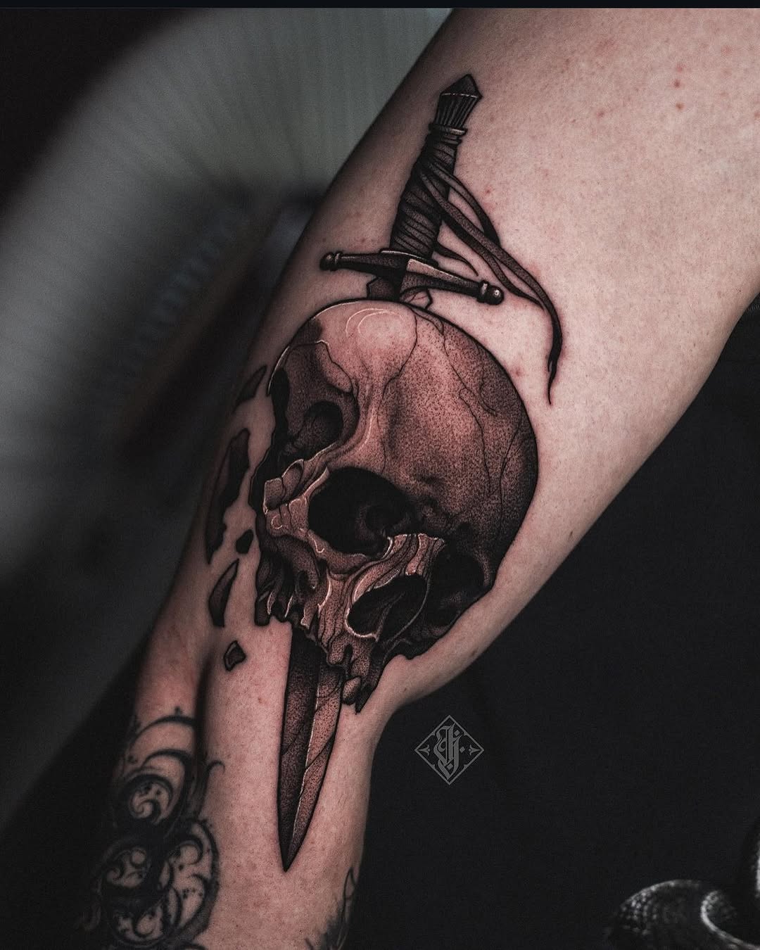 Detailed skull with sword pierced through it and ornate dagger above, rendered in brown and black ink on the forearm.