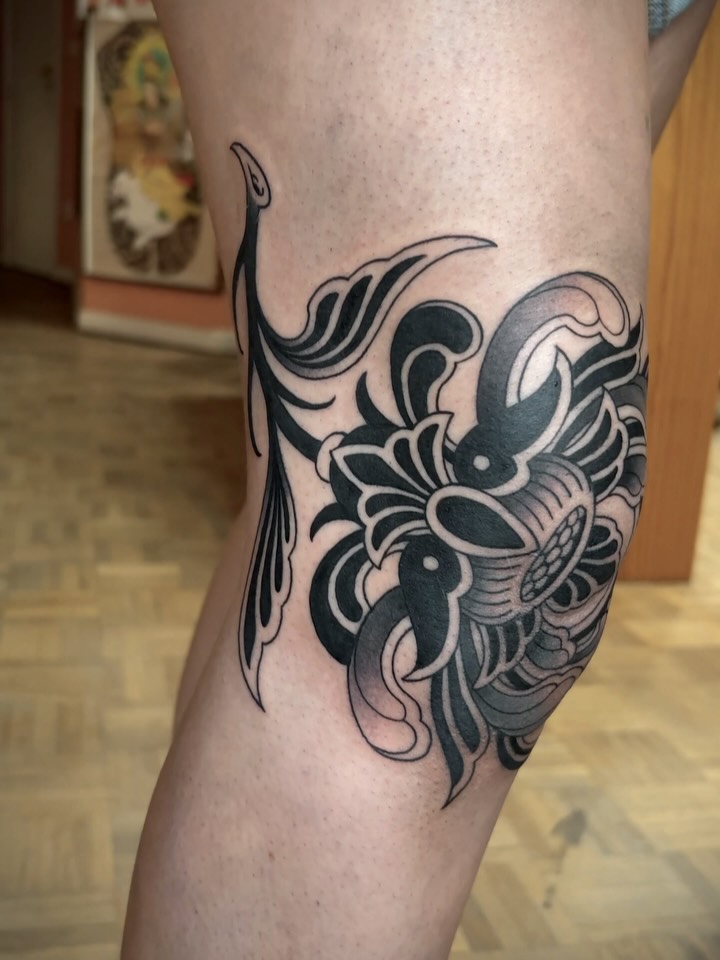 Ornamental elephant head tattoo with flowing curved lines and dotted details on the calf, rendered in black ink with shading.