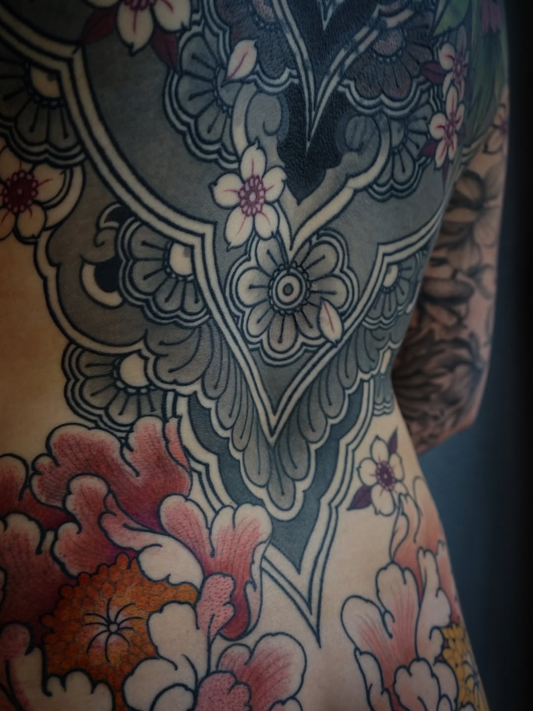 Ornate floral tattoo on thigh featuring blue-grey decorative scrollwork with small flowers, red and orange blooms at the lower portion, and pink petals throughout.