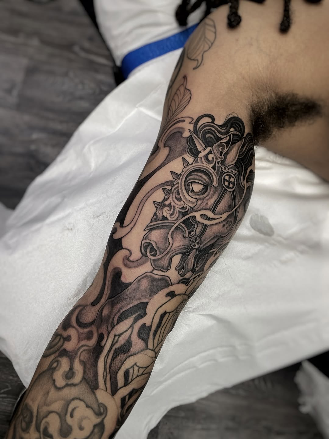 Detailed ornamental arm sleeve tattoo featuring scrollwork, floral motifs, and decorative elements in black and grey ink on the forearm and upper arm.
