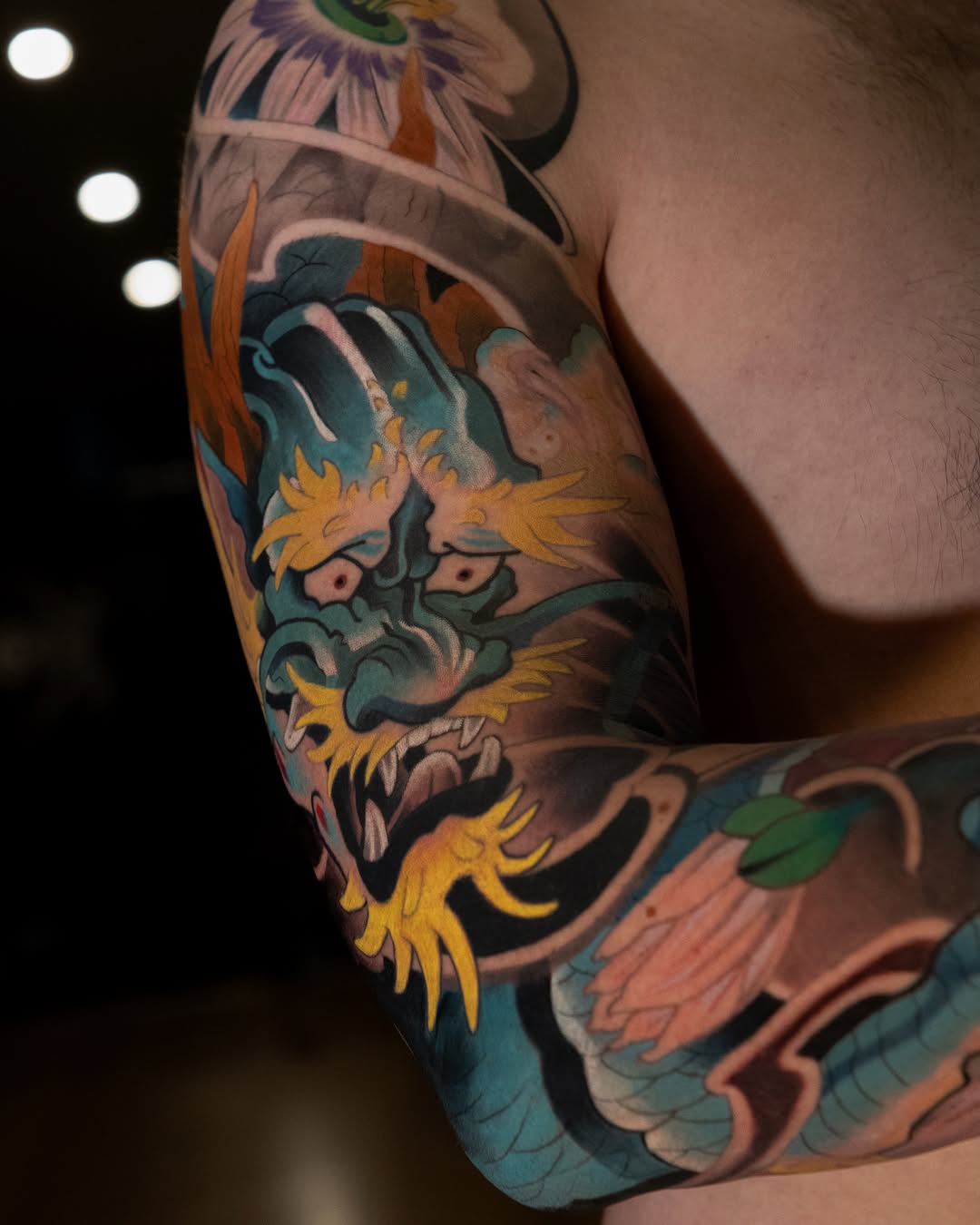 Colorful dragon tattoo on upper arm featuring blue and teal scales, yellow spikes, and orange flame details against skin.