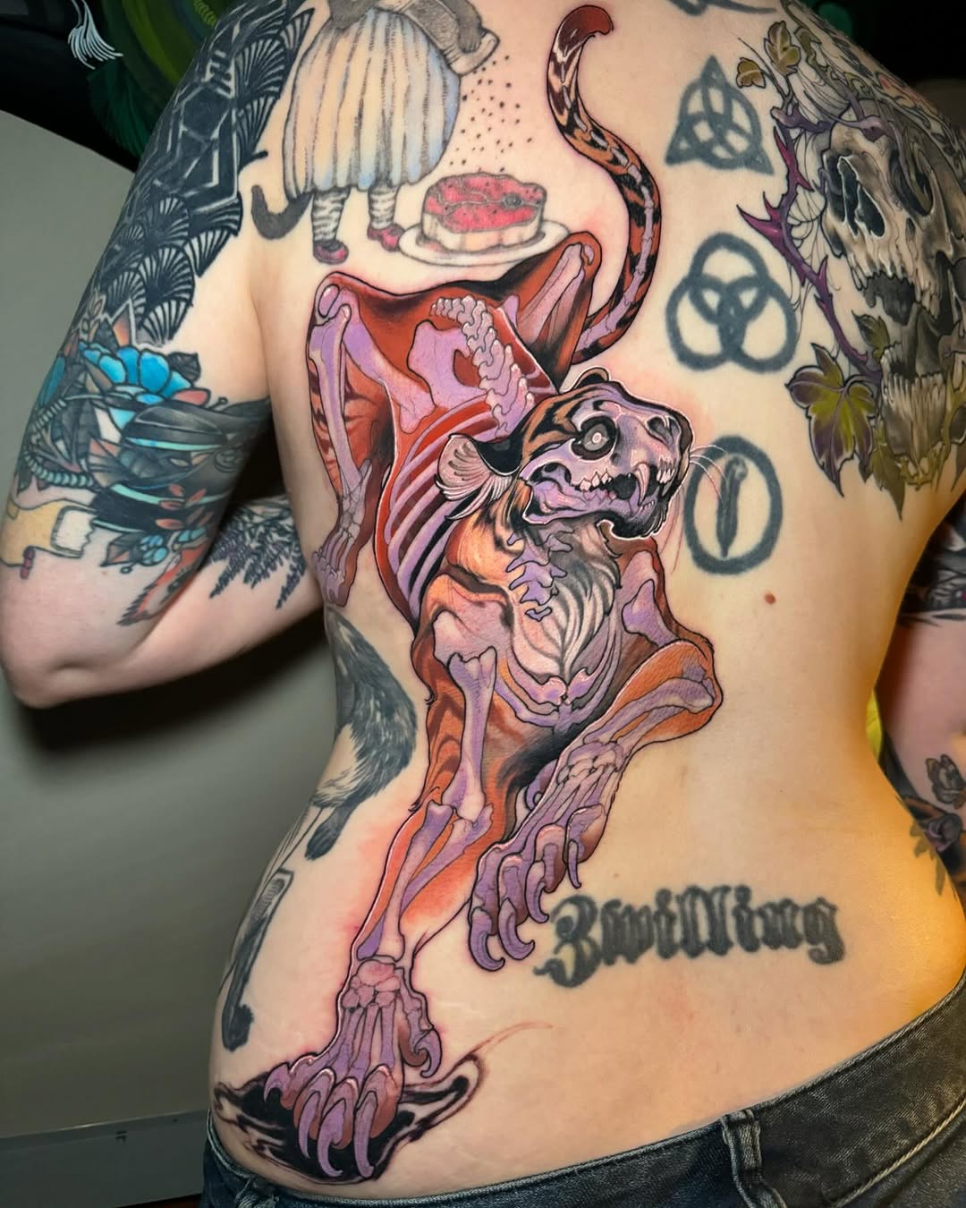 Colorful skeletal demon figure with open mouth and snake, tattooed on torso in red, purple, orange, and pink tones with "Bwuittung" text below.