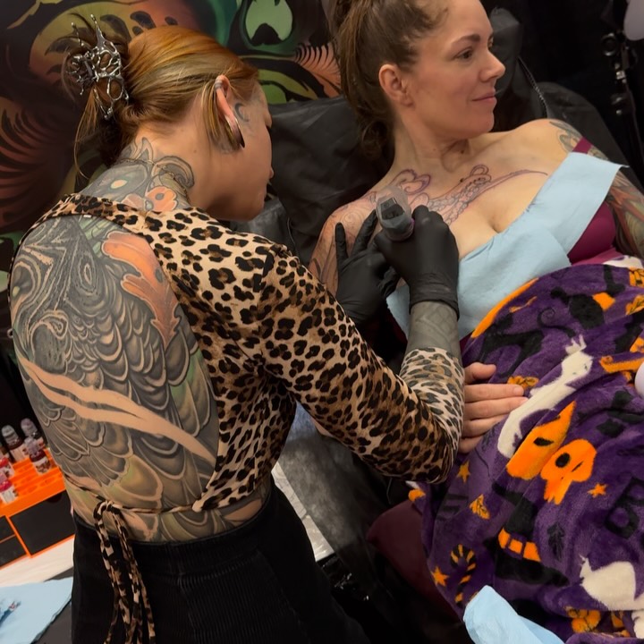 Tattoo artist applying a leopard print sleeve tattoo on a client's arm during a studio session.